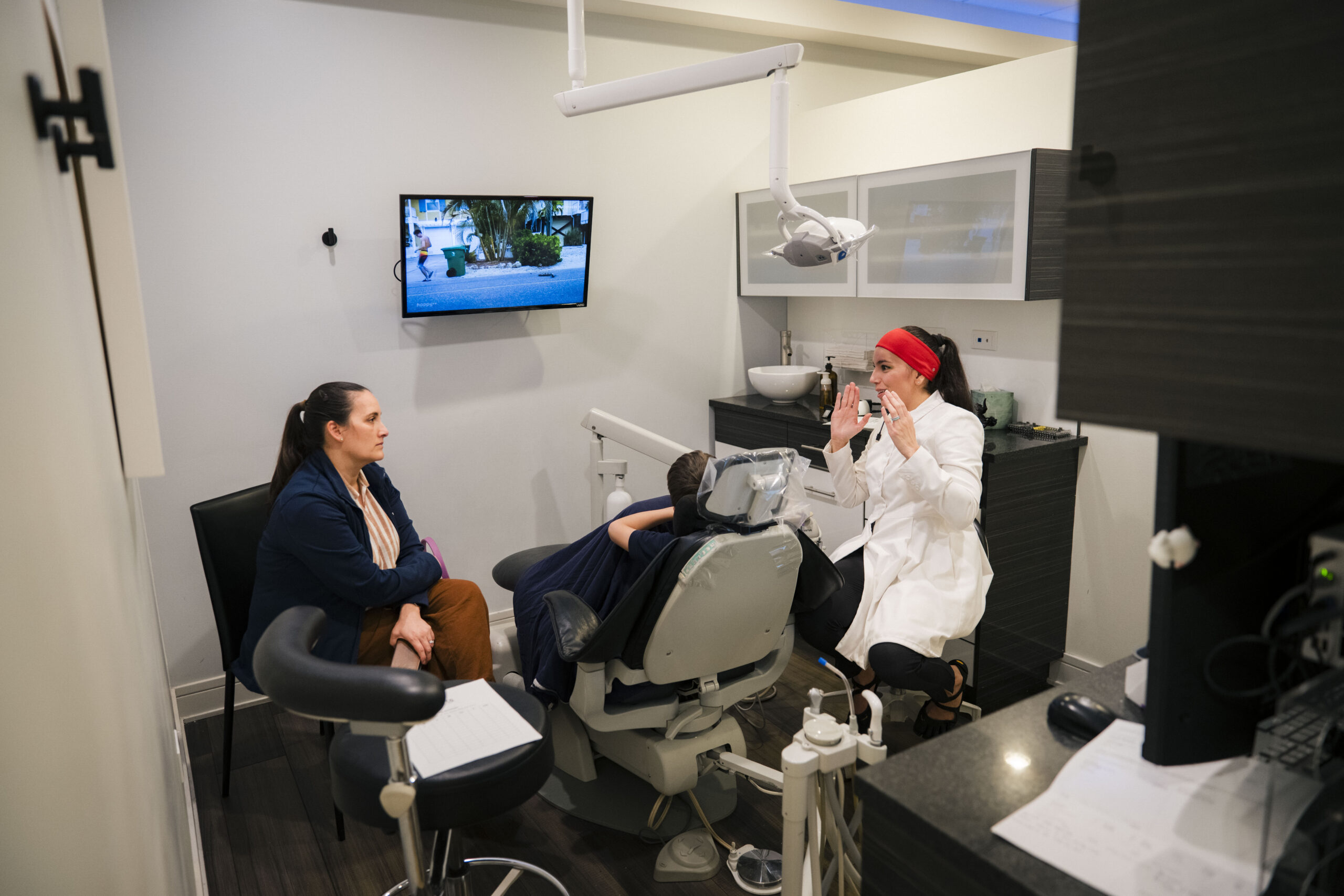 Holistic Airway Dentist consultation: dentist in white coat with red headband discussing treatment with patient in dental cha