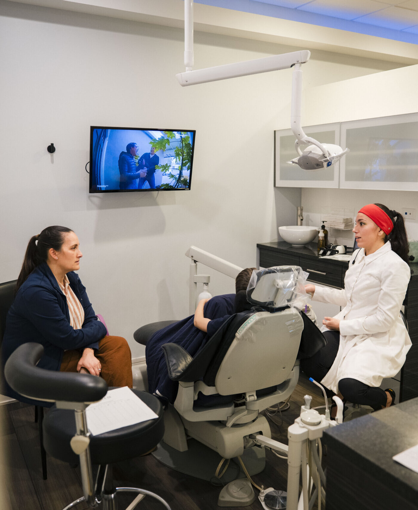 Dentist explaining treatment plan to patient in Holistic Airway Dentist exam room with wall-mounted display.