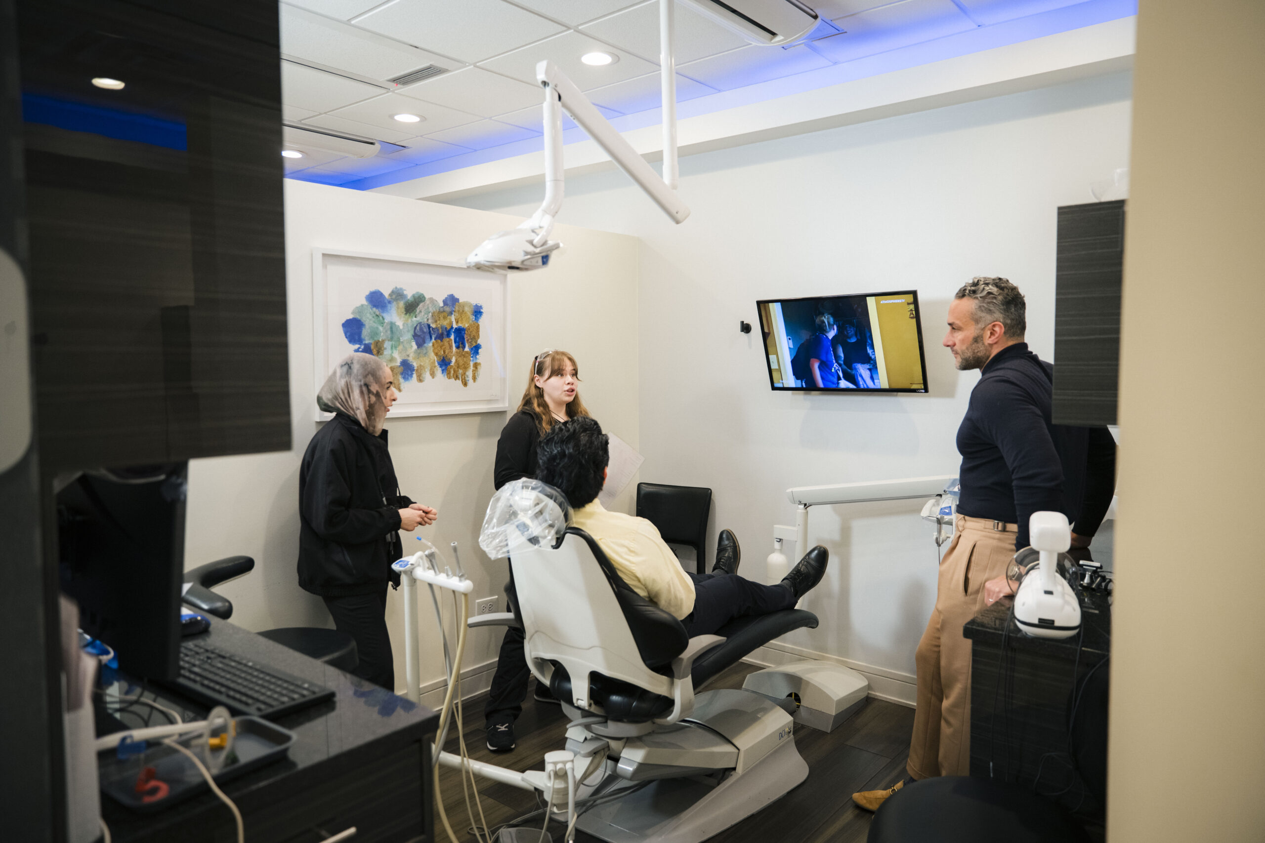 Holistic Airway Dentist team presenting to patient: three staff members in modern treatment room with educational display.
