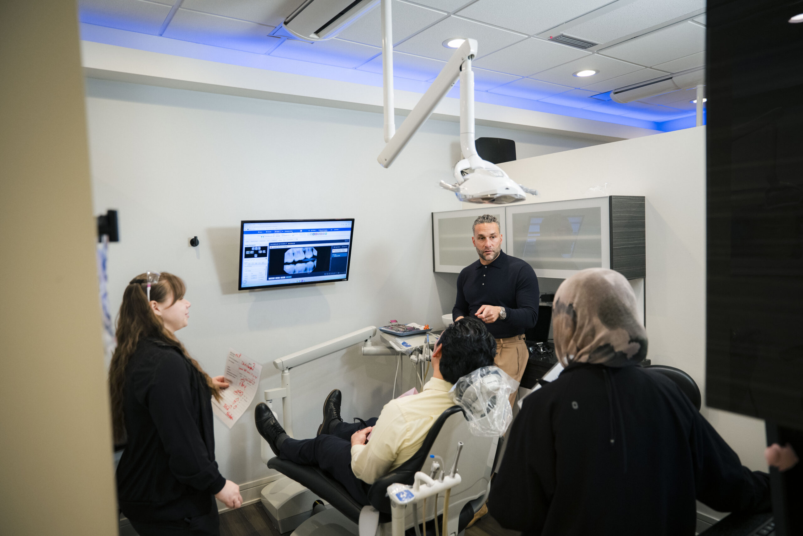 Dentist presenting dental imaging to patients at Holistic Airway Dentist with wall-mounted X-ray display.