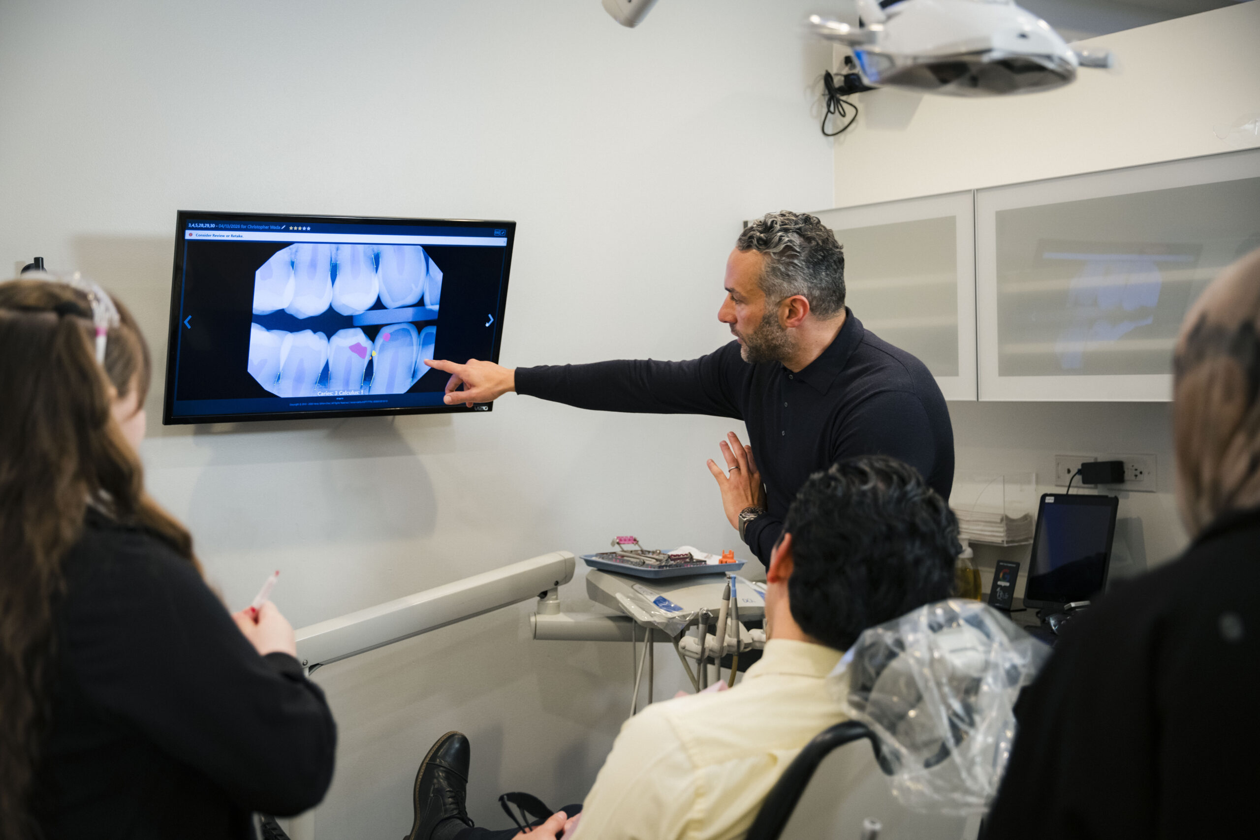 Dentist reviewing digital dental scan with patients on wall monitor in Holistic Airway Dentist office.
