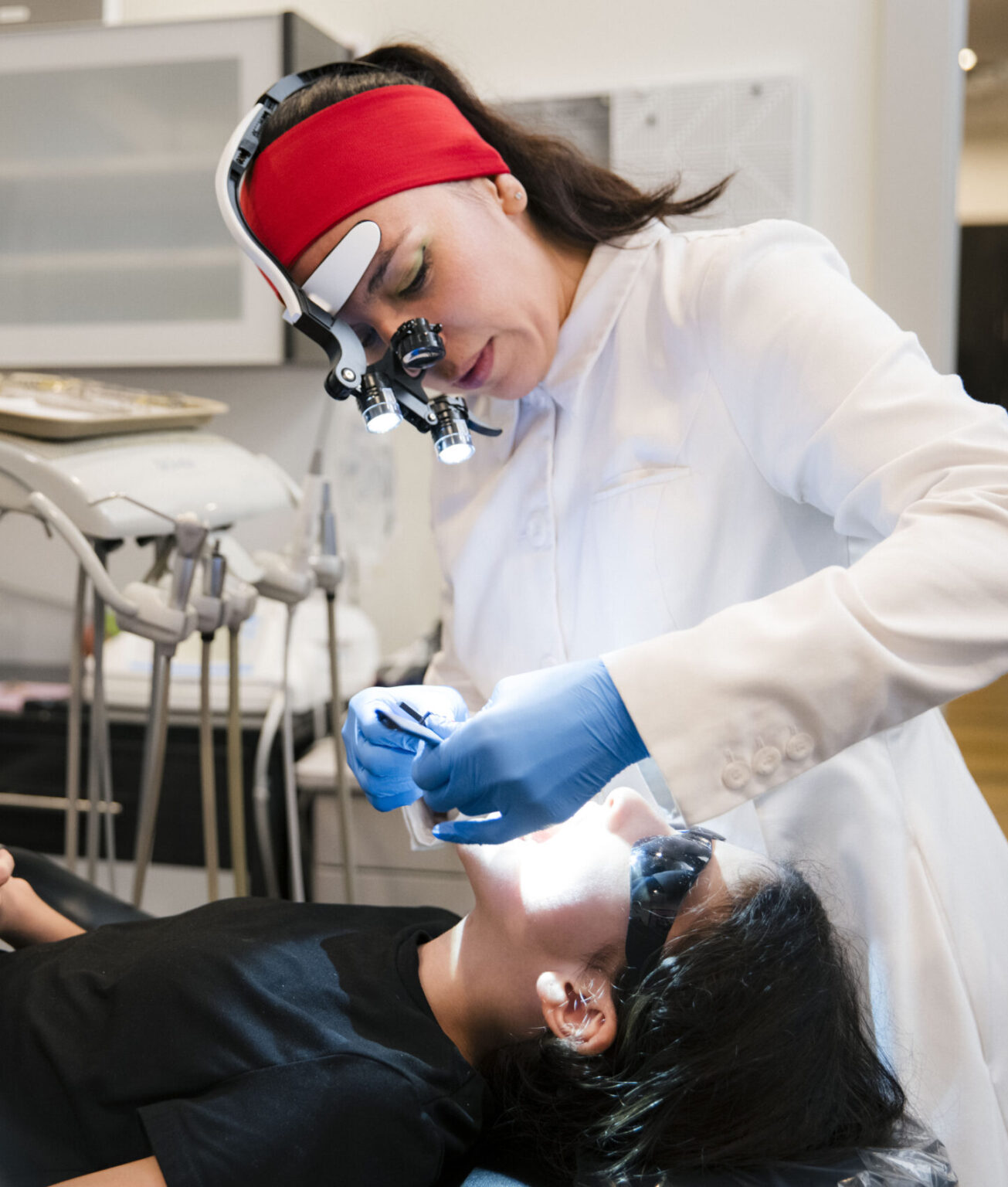Dentist in magnification loupes preparing dental instruments during patient examination in clinical setting