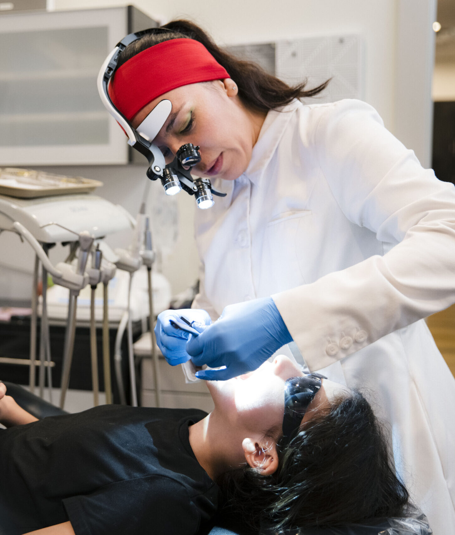Dentist in magnification loupes preparing dental instruments during patient examination in clinical setting