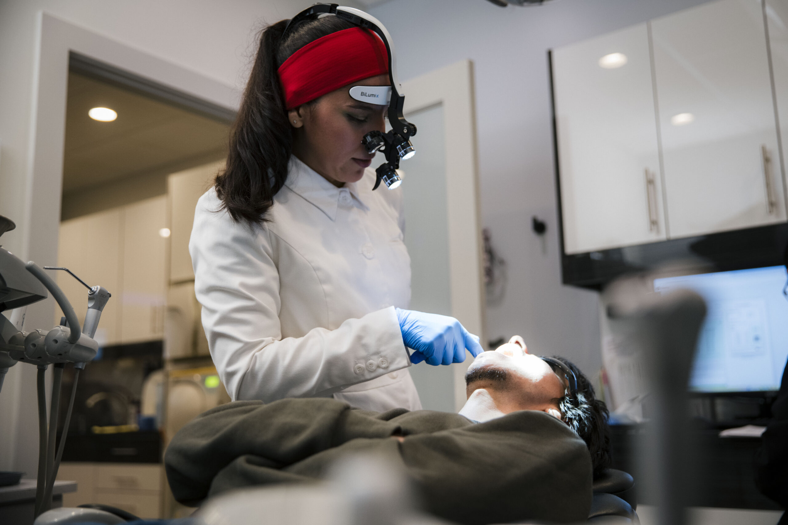 Dentist wearing red headband with magnification loupes performing intraoral examination on patient.